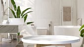 White round side table in modern and luxury design bathroom and tropical banana tree with dappled sunlight from window and leaf shadow on white granite tile wall