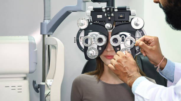 Young woman looking through optical phoropter, checking eye vision with optometrist specializing in clinic.