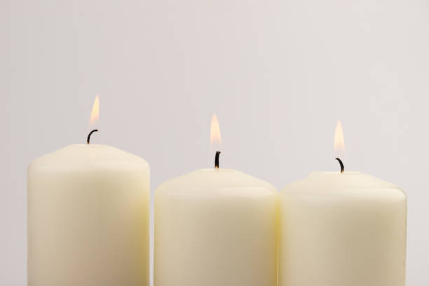 istock Burning white wax candles on white background. 1439695035