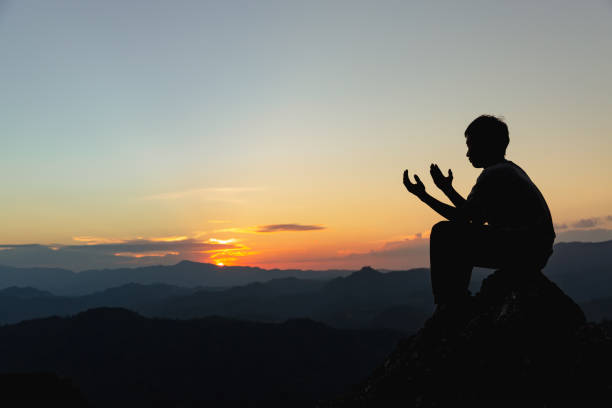 silhouette eines jungen mannes, der auf dem berg bei sonnenuntergang zu gott betet. frau hebt die hände in anbetung. konzept der christlichen religion. - god freedom arms raised high angle view stock-fotos und bilder