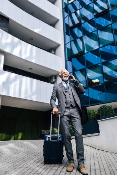 istock Confident entrepreneur with suitcase discussing on smart phone against building. 1439695609