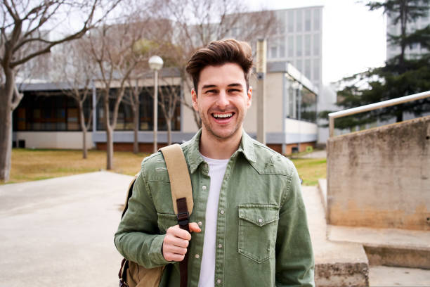 Close up shot of cheerful happy caucasian teenage boy looking at camera smiling. Funny portrait of a young student man with his backpack at campus university. Guy laughing at high school. stock photo