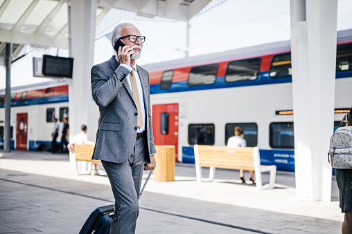 Senior businessman talking on smart phone while walking with luggage at subway station platform during sunny day