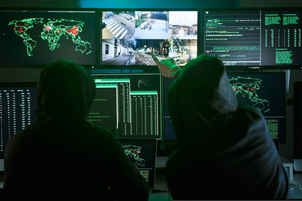 istock Back view of unrecognizable Criminal team Hacker pointing security cameras on screen monitor using computer for organizing massive data breach attack on government or big company servers. Dark room 1439697916