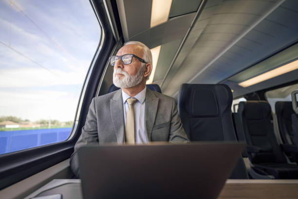 istock Senior thoughtful businessman with laptop looking through window while traveling on passenger train. 1439699278