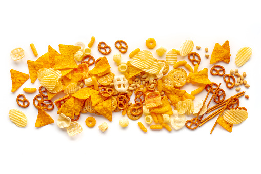Salty snacks texture on a white background. Party food mix. Potato and tortilla chips, crackers and other appetizers, overhead flat lay shot