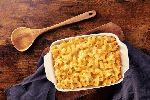 Macaroni and cheese pasta in a casserole dish, oven baked, shot from the top on a rustic background with a wooden spoon