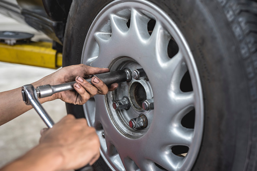 An asian mechanic loosens and removes the lug nuts from the tire of a serviced car with a ratchet lug wrench. Removing a wheel manually. At an auto repair shop.