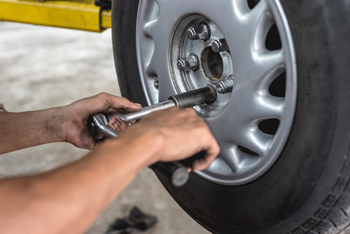 An asian mechanic loosens and removes the lug nuts from the tire of a serviced car with a ratchet lug wrench. Removing a wheel manually. At an auto repair shop.