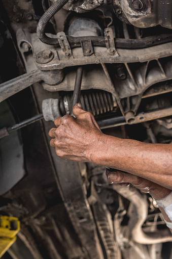 A mechanic inspects the engine support underneath a car, tightening it with a telescoping wrench.