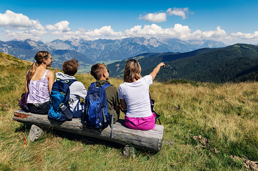 Family is hiking in the Alps - Sazlburg, Austria. They are sitting on a bench high in the mountains and looking at the view.\nCanon R5