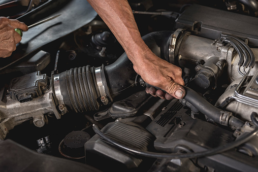 A mechanic loosens the engine intake air duct with his bare hands. At an auto repair shop.