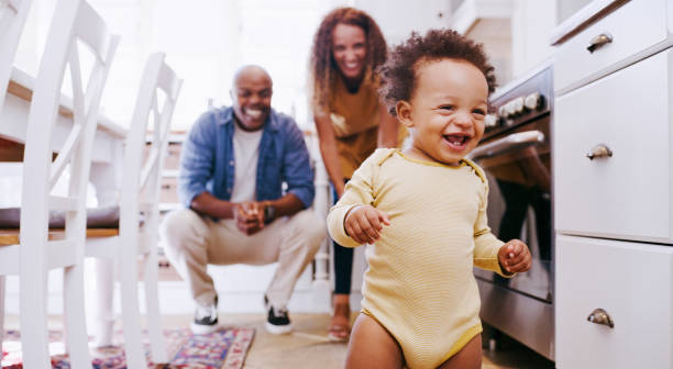 Happy, baby and walking development of a toddler with parents feeling happy, proud and family love. Happiness, laughing and excited first walk of a kid showing growth with mama and father at home stock photo