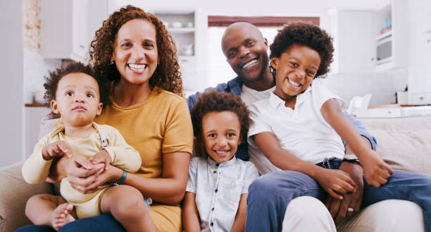 Black family, mother and father with children in the house living room relaxing and bonding on a sofa together. Portrait, mama and dad enjoying quality time with happy African kids, siblings and boys stock photo