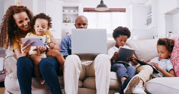 Relax, happy and technology with family on sofa for learning, social media and internet. Website, digital and and app with parents and children in living room at home with laptop, phone and tablet stock photo