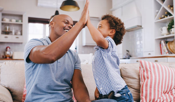 istock Father, child and high five for winning video game on sofa in learning achievement, celebration and support. Black family dad and kid with success hand sign for television gaming development on couch 1439704827