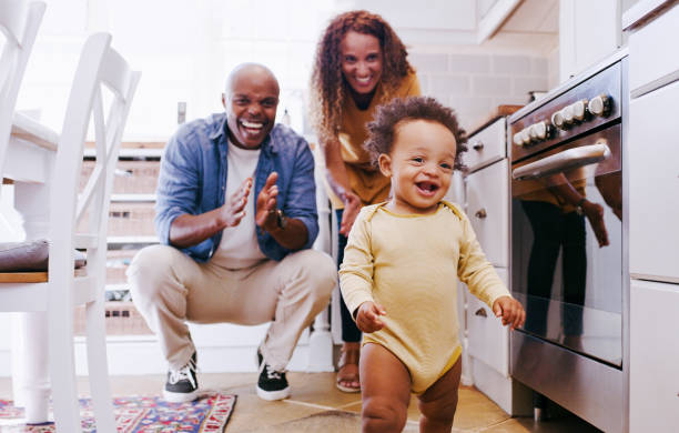 Happy, walking baby and proud parents in a home kitchen with a smile about black family bonding. Happiness, celebration and toddler spending quality time with mama and father in a house together stock photo