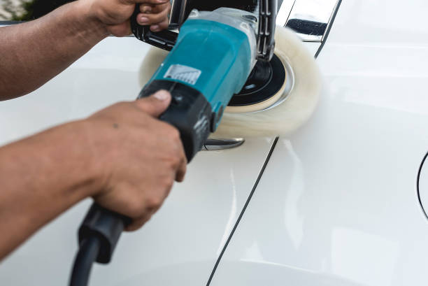 A man polishing the surface of the door of a white sedan with an electric buffing machine. At an auto detailing shop. A man polishing the surface of the door of a white sedan with an electric buffing machine. At an auto detailing shop. car Power Waxer stock pictures, royalty-free photos & images