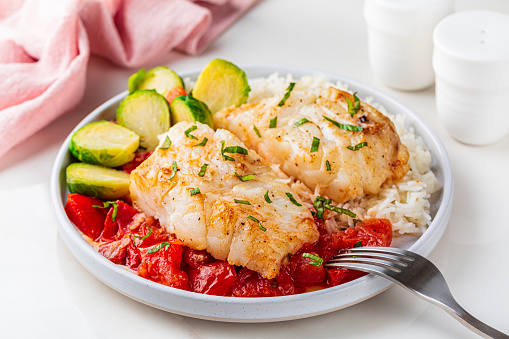 Baked cod fish, with tomato, brussel sprouts and boiled rice. Balanced food concept.