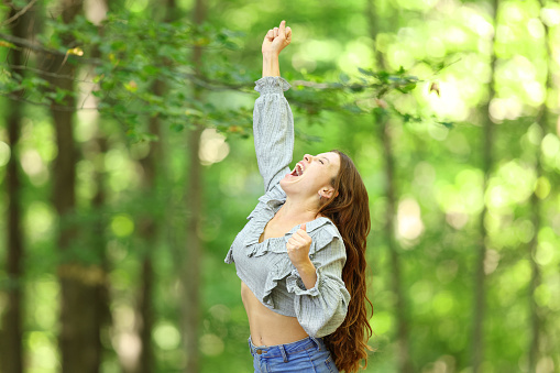 Euphoric woman celebrating in a forest raising arm