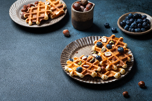 Freshly made belgian waffles with blueberry and hazelnut. Waffles with honey and berry. Place for text. Copy space. Classic sweet breakfast.