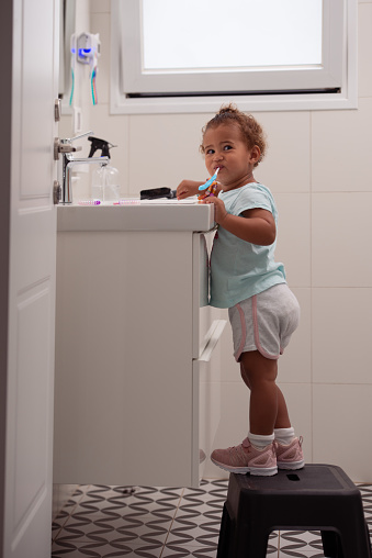 Cute child brushing teeth, making faces,  standing in the bathroom on a baby step stool.