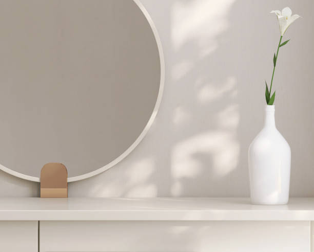 Minimal, modern and contemporary design of creamed colored dressing table with round vanity mirror, vase of flower in dappled sunlight from window in white wall bedroom