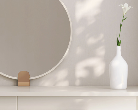 Minimal, modern and contemporary design of creamed colored dressing table with round vanity mirror, vase of flower in dappled sunlight from window in white wall bedroom for beauty and personal care product display