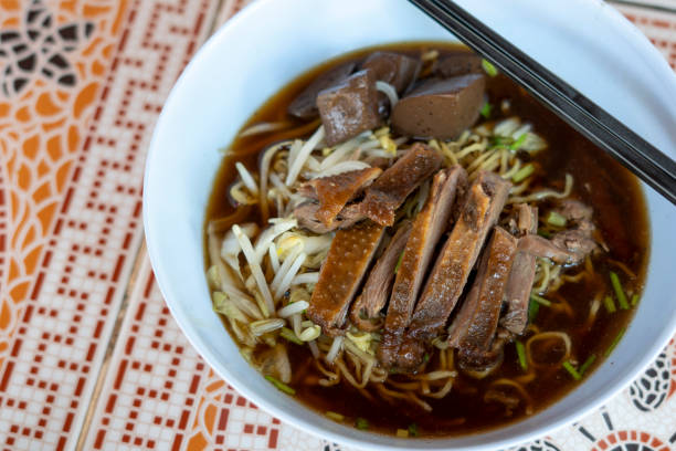 A close-up view of a bowl of soba noodles, traditionally eaten as Toshikoshi Soba on New Year's Eve in Japan to wish for longevity and to let go of past hardships. The dish features dark buckwheat noodles topped with succulent, sliced duck breast, fresh green onions, and delicate green herbs. The soba can be served hot in a savory broth or with a dipping sauce, like Kamo Seiro style.