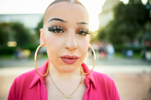 Headshot of 20 year old with hair slicked back wearing big hoop earrings, false eyelashes, hot pink dress, and looking at camera with serious expression.