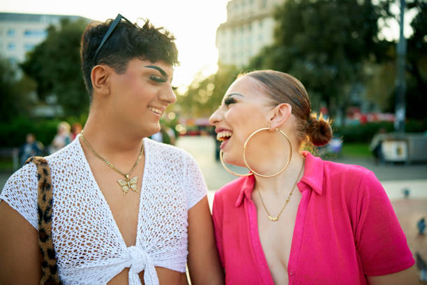 Barcelona friends talking and laughing outdoors at dusk Candid head and shoulders portrait of young woman in bright pink dress and big hoop earrings face to face with gay teenage friend at Plaça de Catalunya. Crossdresser Posing stock pictures, royalty-free photos & images