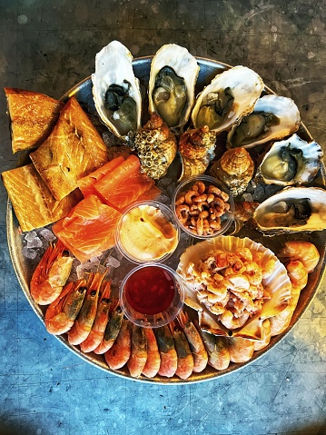 Fresh platter of seafood - including oysters, shrimp, prawns and whelks - on a metallic surface. Overhead view with copy space.