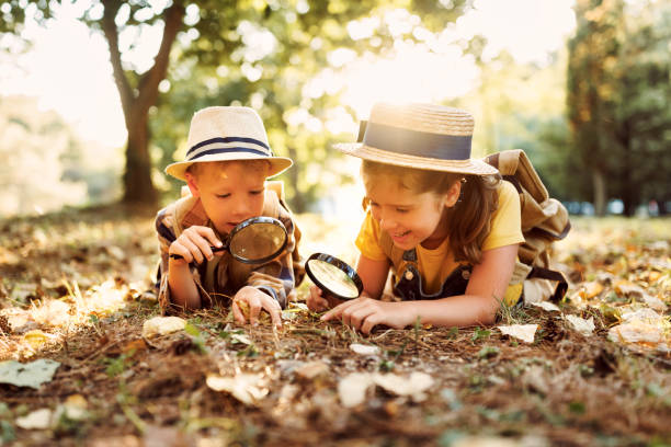istock Two little kids with backpacks examining plants through magnifying glass in forest 1439715365