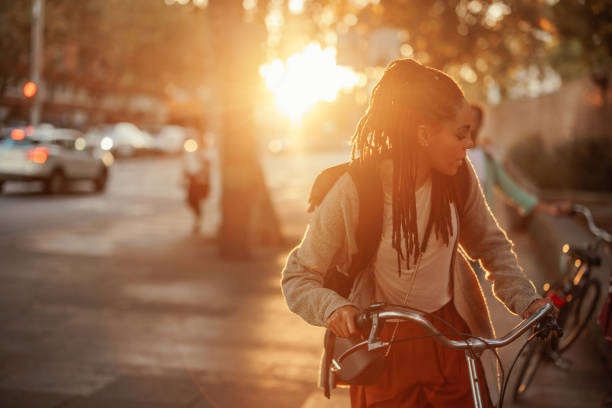 A young African American woman is in a city with her bicycle with a beautiful sunset behind her and copy space.
