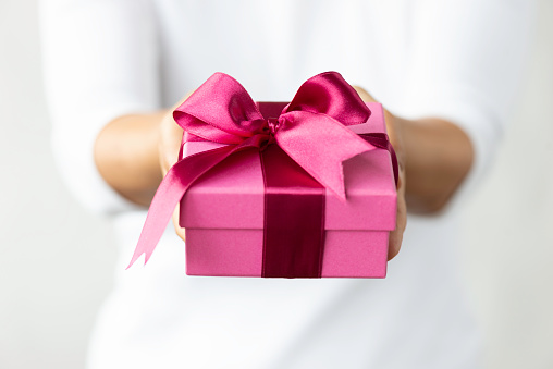 Chest view of an unrecognizable caucasian female wearing a white t-shirt who is about to give a pink gift box