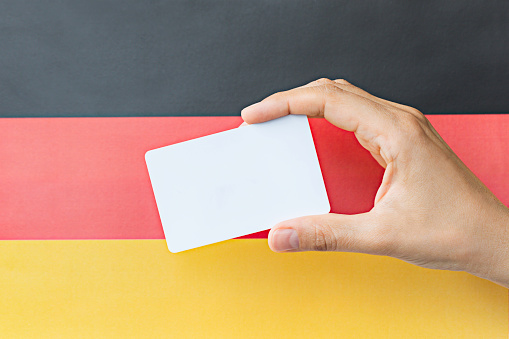 Hand holding blank card in front of flag of Germany. Representing identity and citizenship concept.