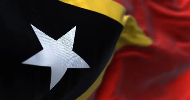 Close-up view of East Timor National flag waving. The Democratic Republic of East Timor is a country in Southeast Asia. Fabric textured background. Selective focus. 3D illustration render