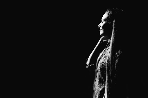 Long-haired beautiful woman lit by direct sunlight on a black background