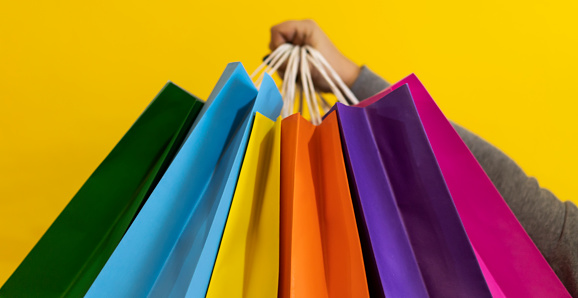 Close-up of a woman's hands holding colorful shopping bags.