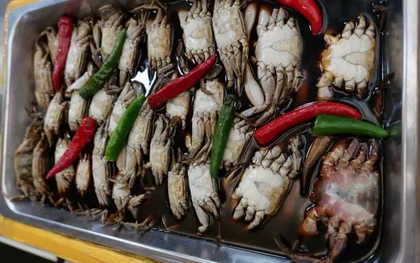 Metal tray of crabs marinating in soy sauce with red and green chillis