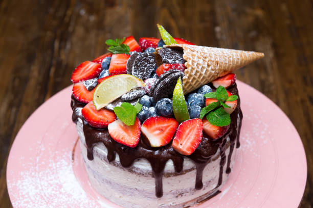 Fresh berries on a chocolate topping on a homemade cake. Birthday cake on a pink cake stand. With lime slices and mint leaves, brown cookies and powdered sugar on top. stock photo