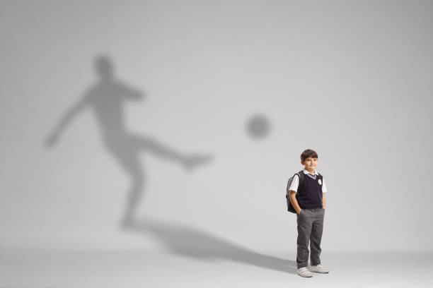 istock Schoolboy in a uniform posing with a football player shadow 1439731267