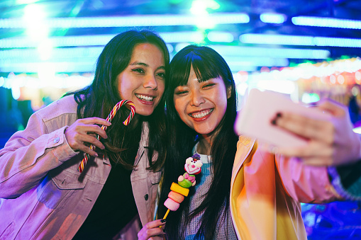 Chicas asiáticas felices divirtiéndose haciendo selfies al aire libre en un parque de diversiones - Focus on right girl face photo