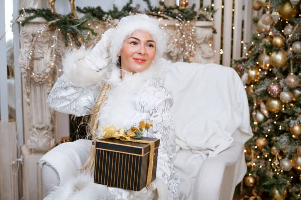snow maiden sosteniendo. regalo mientras está sentado en una silla junto al árbol de navidad - ice maiden fotografías e imágenes de stock