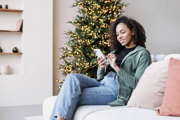 istock Young woman on sofa using smartphone, relaxing at home during holidays 1439734759