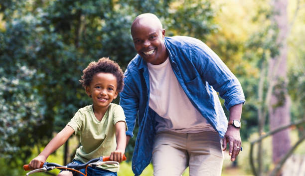 Child learning, black man and kid with bicycle, training or learning to ride with smile, happy or excited for growth. Development, dad and boy practice riding bike, bonding or loving together outdoor stock photo