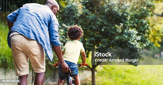 istock Child learning, black man and kid with bicycle, training or learning to ride. Development, dad and boy practice riding bike, bonding or loving together in park or nature 1439735728