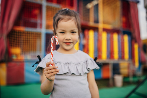 One girl, portrait of a cute little girl holding a candy cane at the modern playground outdoors.