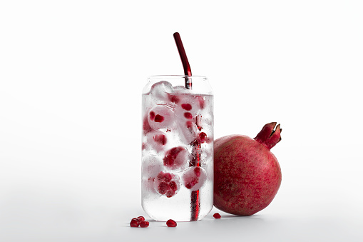 glass of ice water with pomegranate seeds isolated on white background