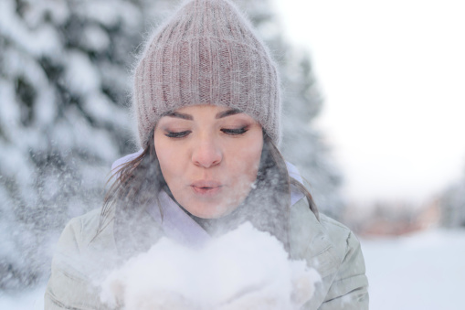 Young beautiful woman blowing snow off the hand.Winter outdoor activity, winter holidays.Selective focus, close up.